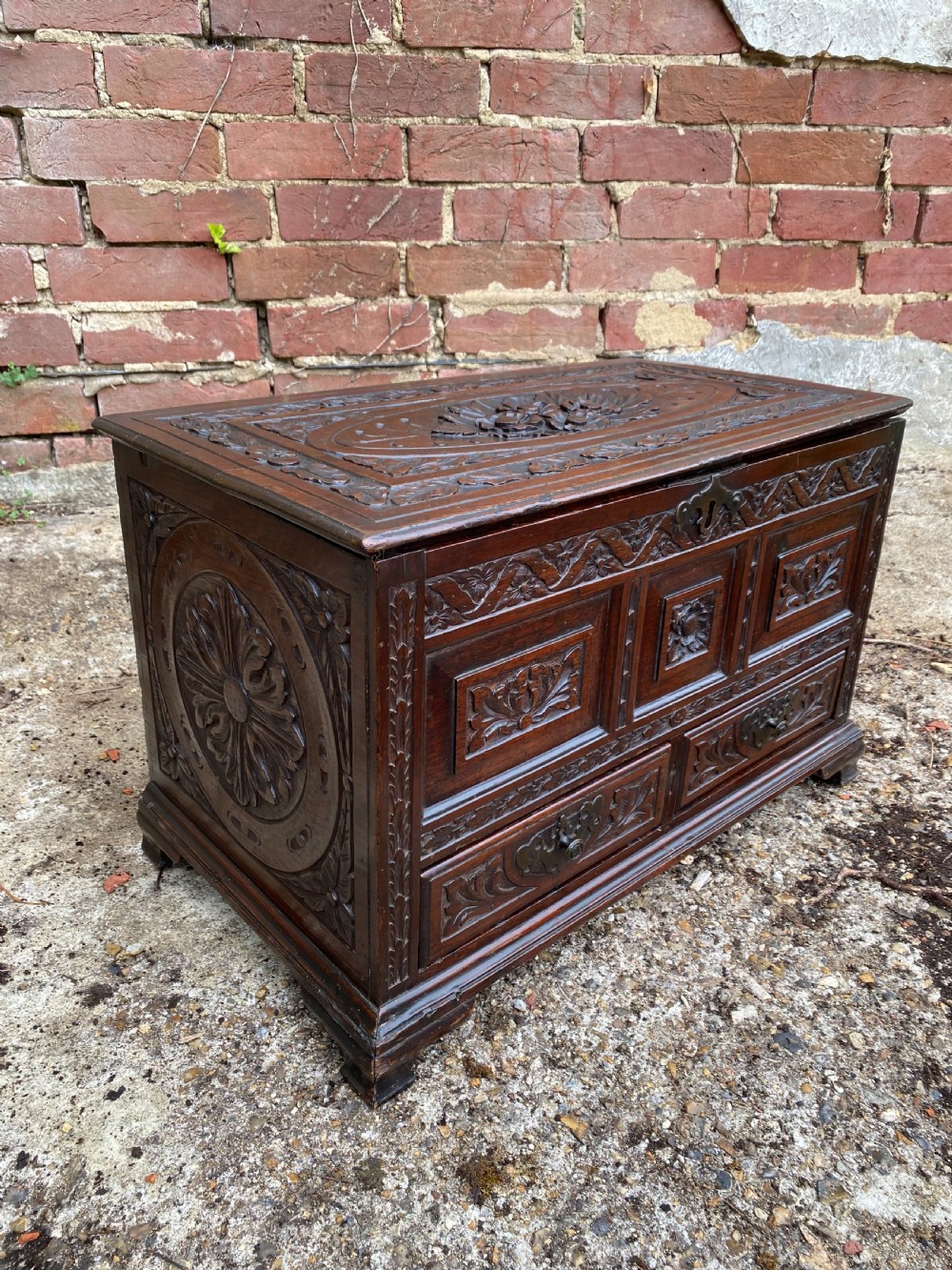 A carved dark oak Georgian coffer bach featuring a hinged lid, relief-carved floral panels, two lower drawers, and bracket feet. View XI