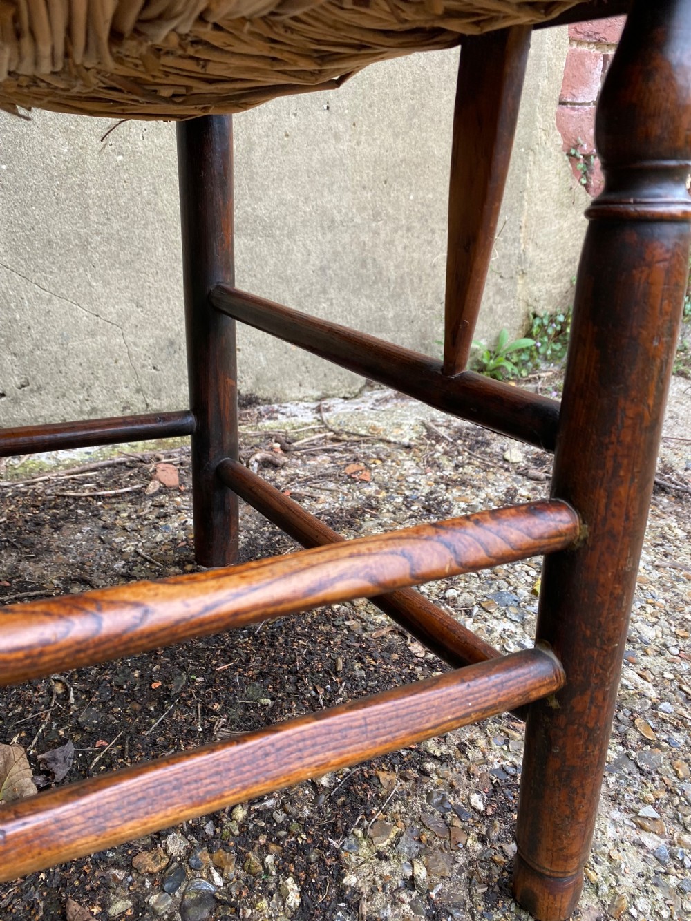 A dark wood Arts and Crafts Sussex armchair featuring a turned spindle backrest, curved armrests, and a woven rush seat. View VIII