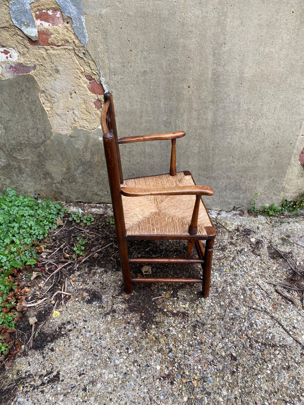 A dark wood Arts and Crafts Sussex armchair featuring a turned spindle backrest, curved armrests, and a woven rush seat. View XII
