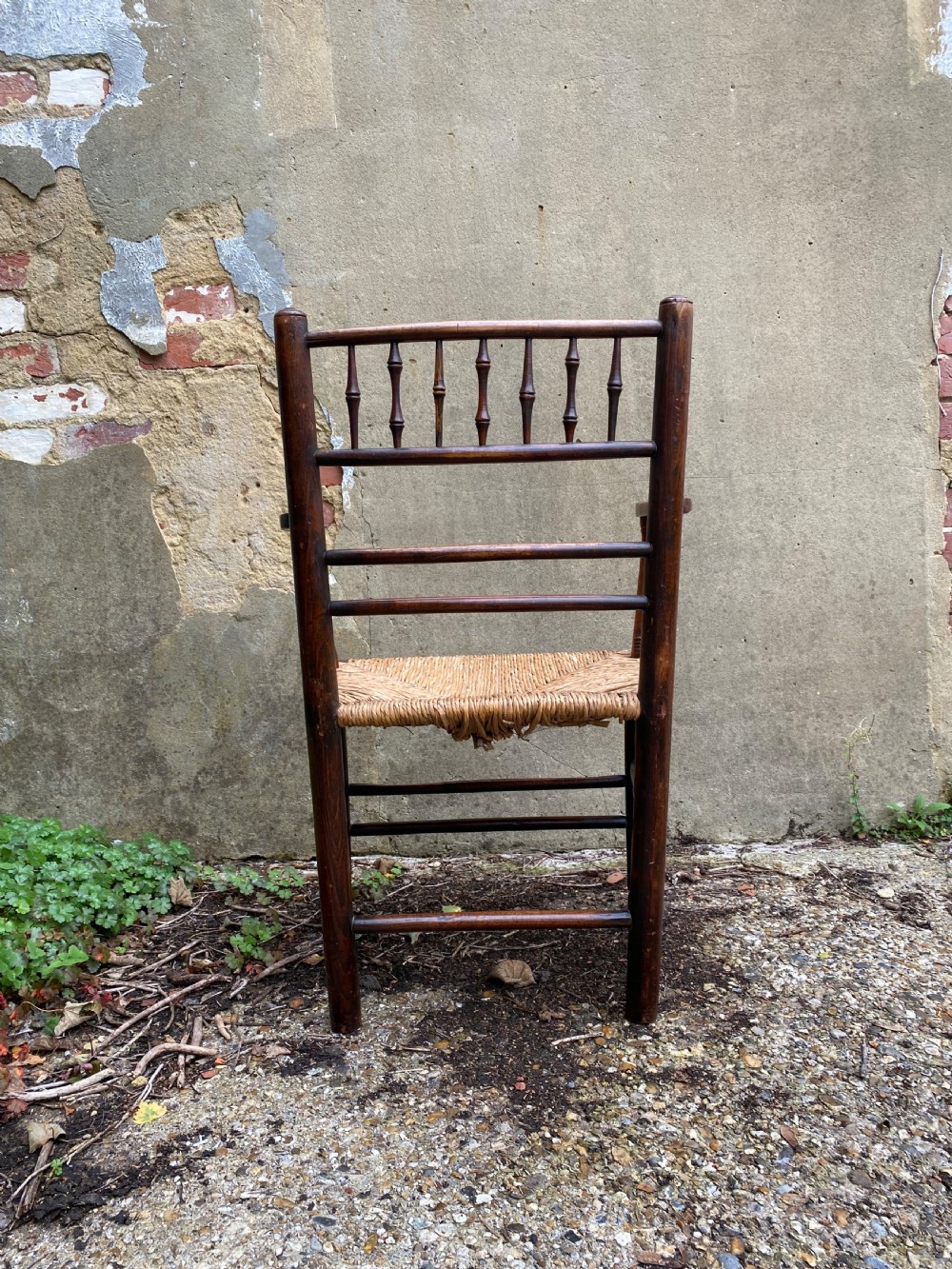 A dark wood Arts and Crafts Sussex armchair featuring a turned spindle backrest, curved armrests, and a woven rush seat. View XIII