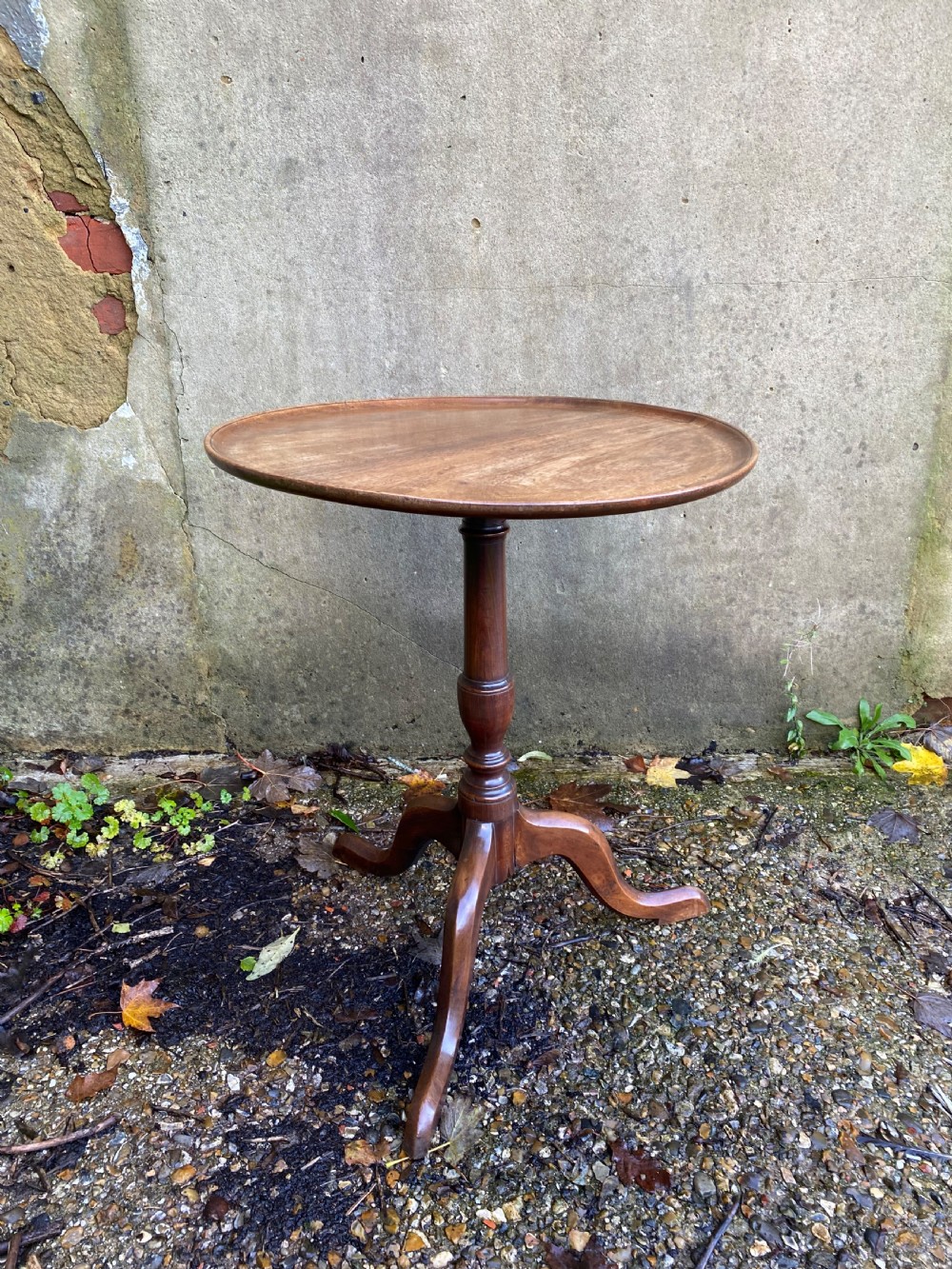 A Georgian mahogany circular side table featuring a dished top, a turned central column, and three tripod cabriole legs.
