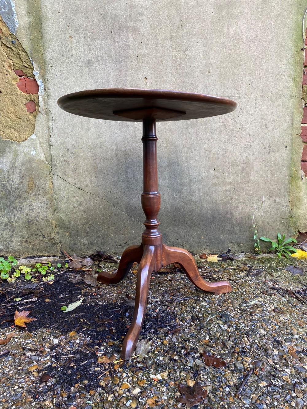 A Georgian mahogany circular side table featuring a dished top, a turned central column, and three tripod cabriole legs. View II