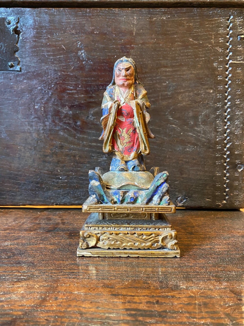 A small hand-carved wooden deity figure with polychrome painted robes and gilt detailing, standing on a carved tiered base.