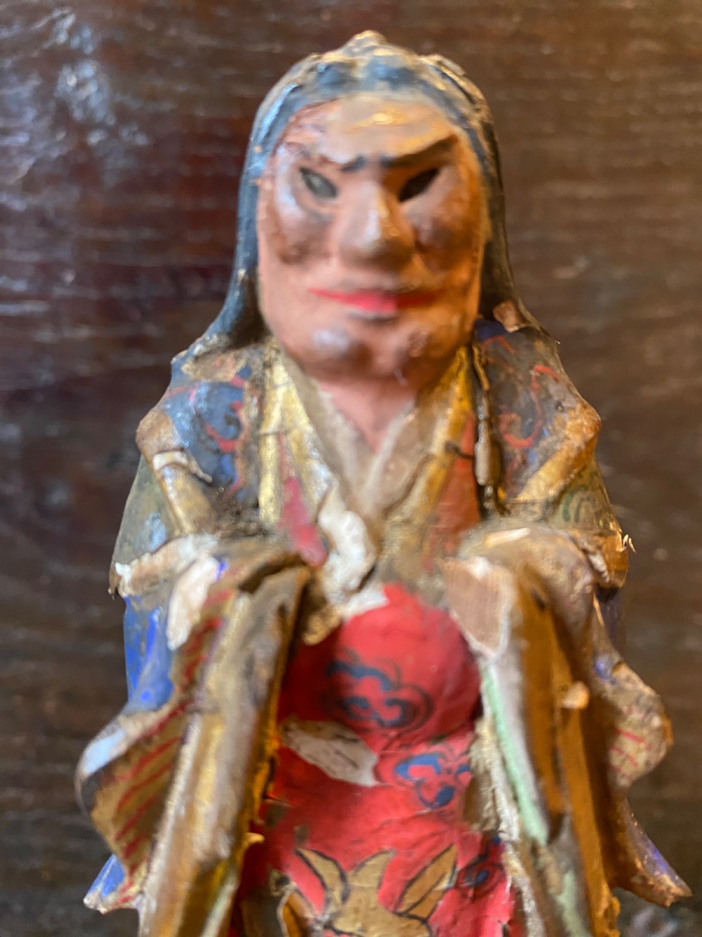 A small hand-carved wooden deity figure with polychrome painted robes and gilt detailing, standing on a carved tiered base. View II