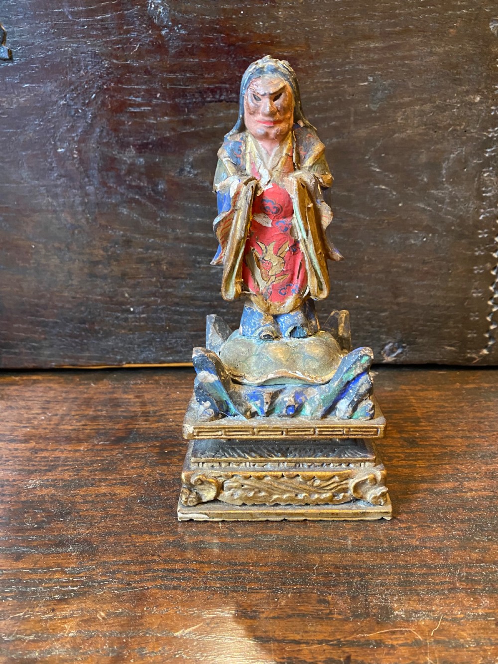 A small hand-carved wooden deity figure with polychrome painted robes and gilt detailing, standing on a carved tiered base. View IV
