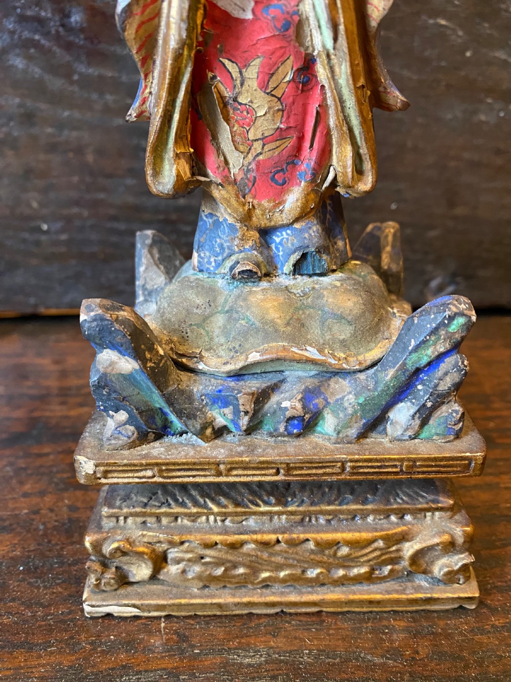 A small hand-carved wooden deity figure with polychrome painted robes and gilt detailing, standing on a carved tiered base. View V