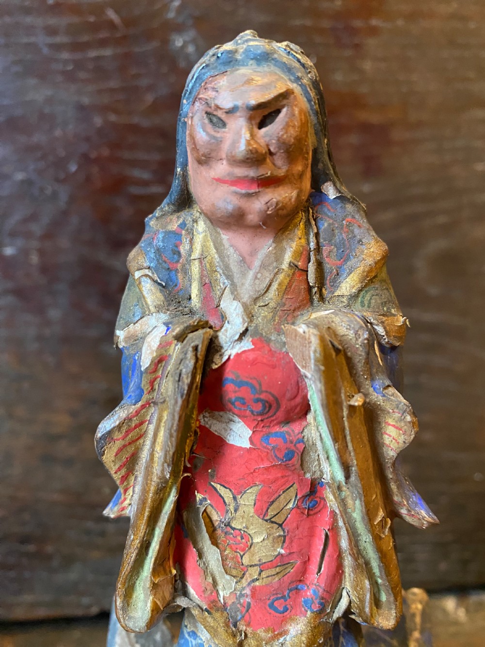 A small hand-carved wooden deity figure with polychrome painted robes and gilt detailing, standing on a carved tiered base. View VIII