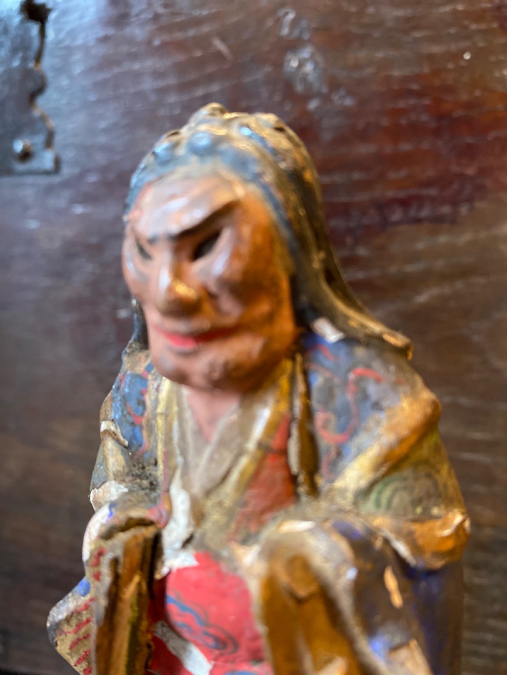 A small hand-carved wooden deity figure with polychrome painted robes and gilt detailing, standing on a carved tiered base. View IX