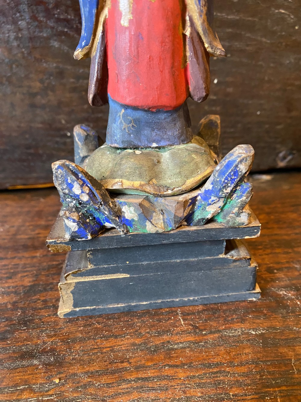 A small hand-carved wooden deity figure with polychrome painted robes and gilt detailing, standing on a carved tiered base. View XIII