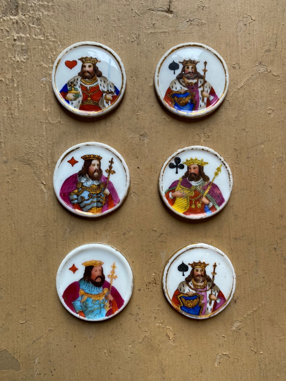 A set of six circular white porcelain gaming tokens decorated with hand-painted playing card king figures and cursive script lettering. View II