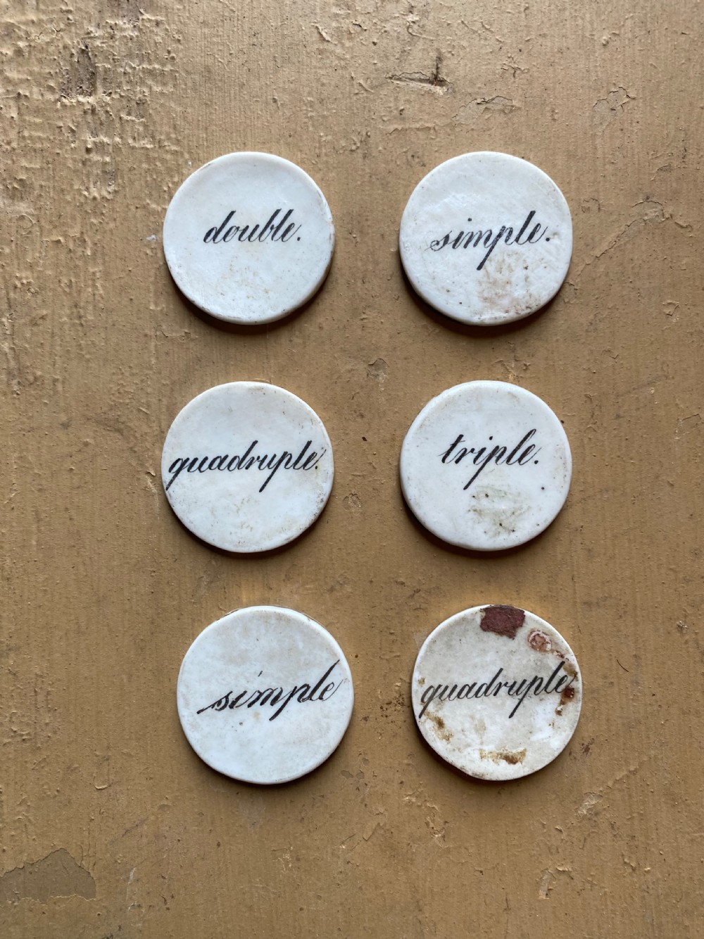 A set of six circular white porcelain gaming tokens decorated with hand-painted playing card king figures and cursive script lettering. View III