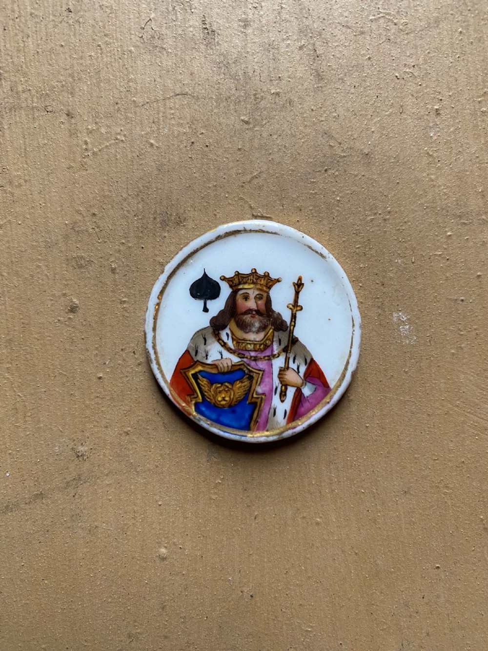A set of six circular white porcelain gaming tokens decorated with hand-painted playing card king figures and cursive script lettering. View VI