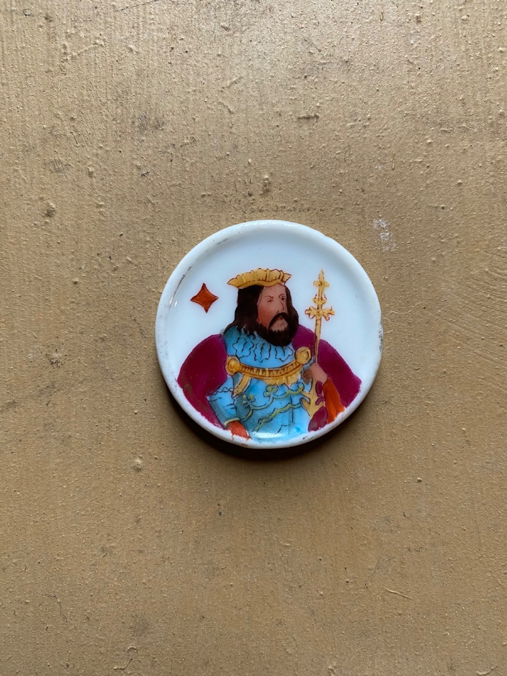 A set of six circular white porcelain gaming tokens decorated with hand-painted playing card king figures and cursive script lettering. View IX