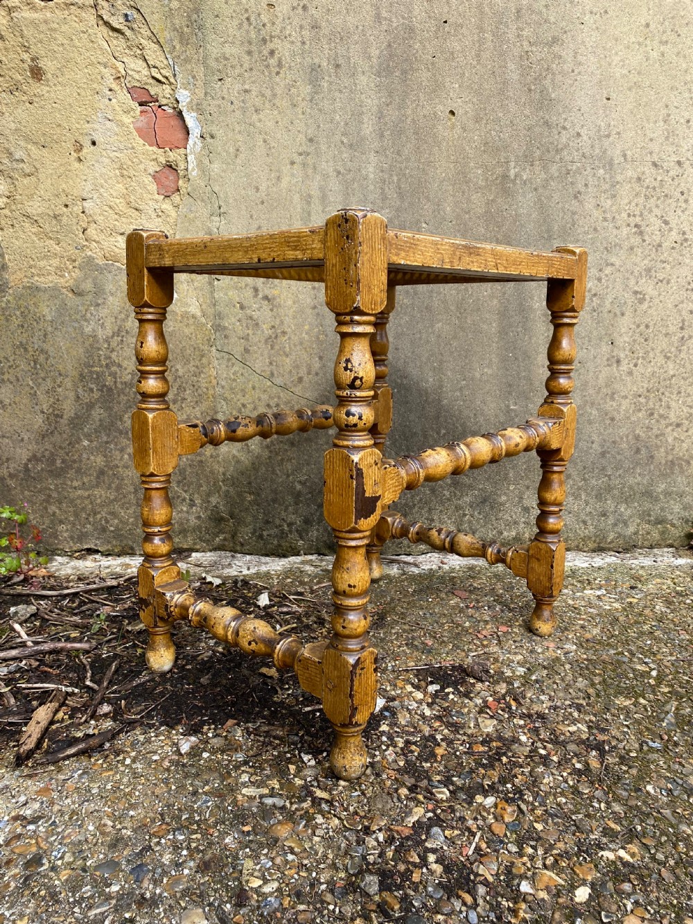 A rectangular wooden stool featuring turned bobbin legs, horizontal stretchers, and a woven cane seat panel with a distressed warm brown finish.