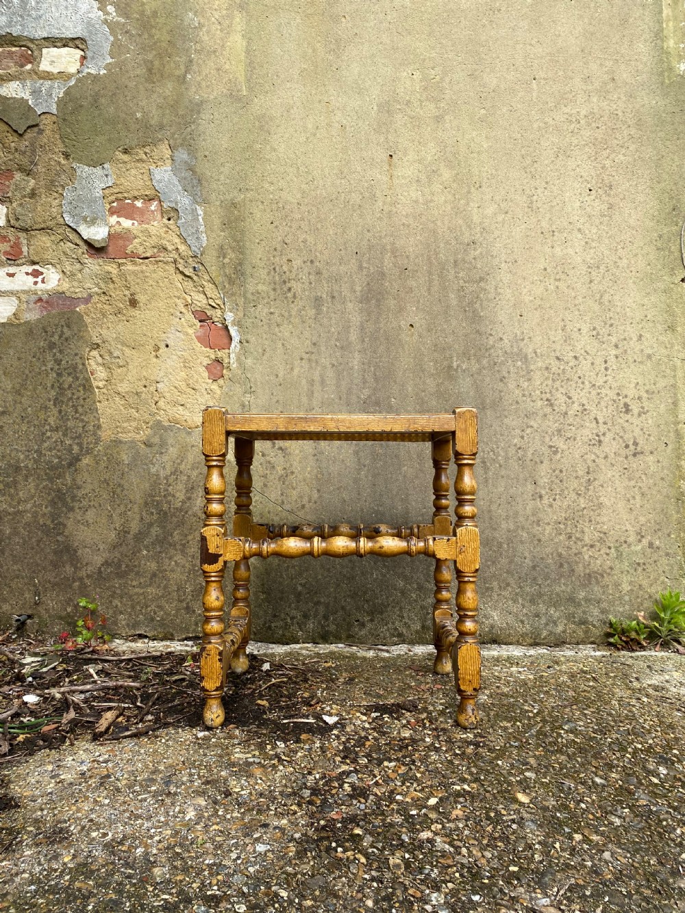 A rectangular wooden stool featuring turned bobbin legs, horizontal stretchers, and a woven cane seat panel with a distressed warm brown finish. View II