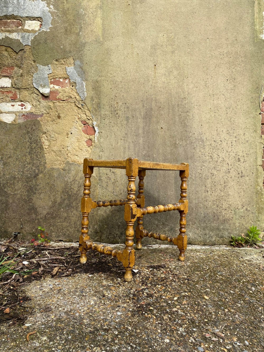 A rectangular wooden stool featuring turned bobbin legs, horizontal stretchers, and a woven cane seat panel with a distressed warm brown finish. View VII