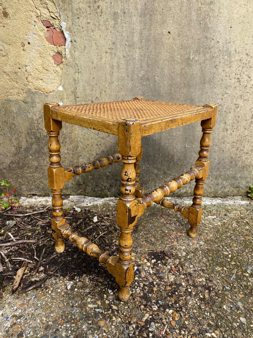A rectangular wooden stool featuring turned bobbin legs, horizontal stretchers, and a woven cane seat panel with a distressed warm brown finish. View VIII