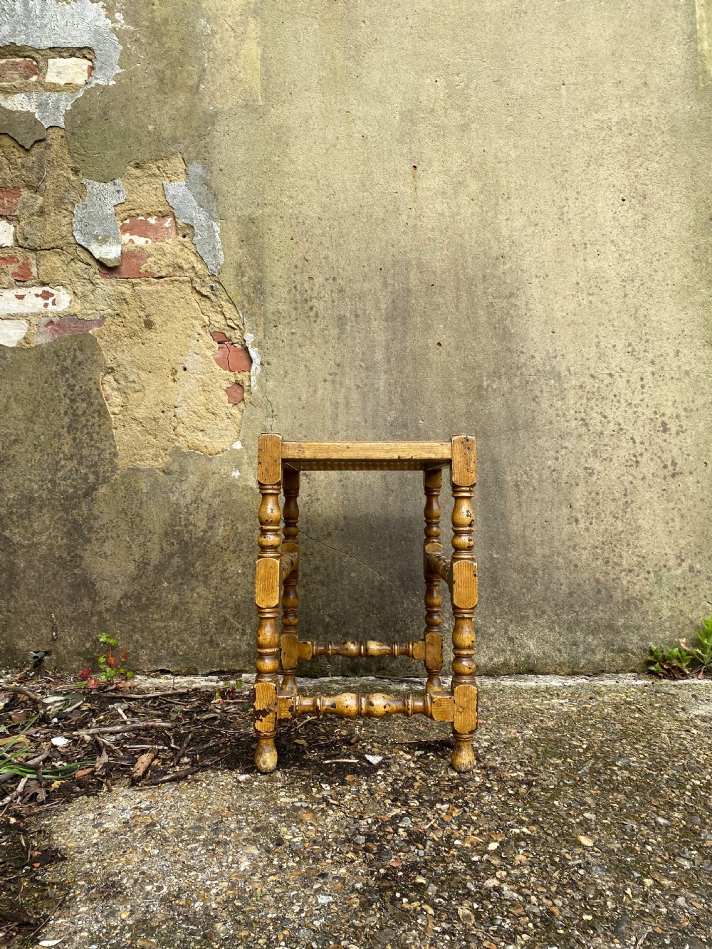 A rectangular wooden stool featuring turned bobbin legs, horizontal stretchers, and a woven cane seat panel with a distressed warm brown finish. View IX