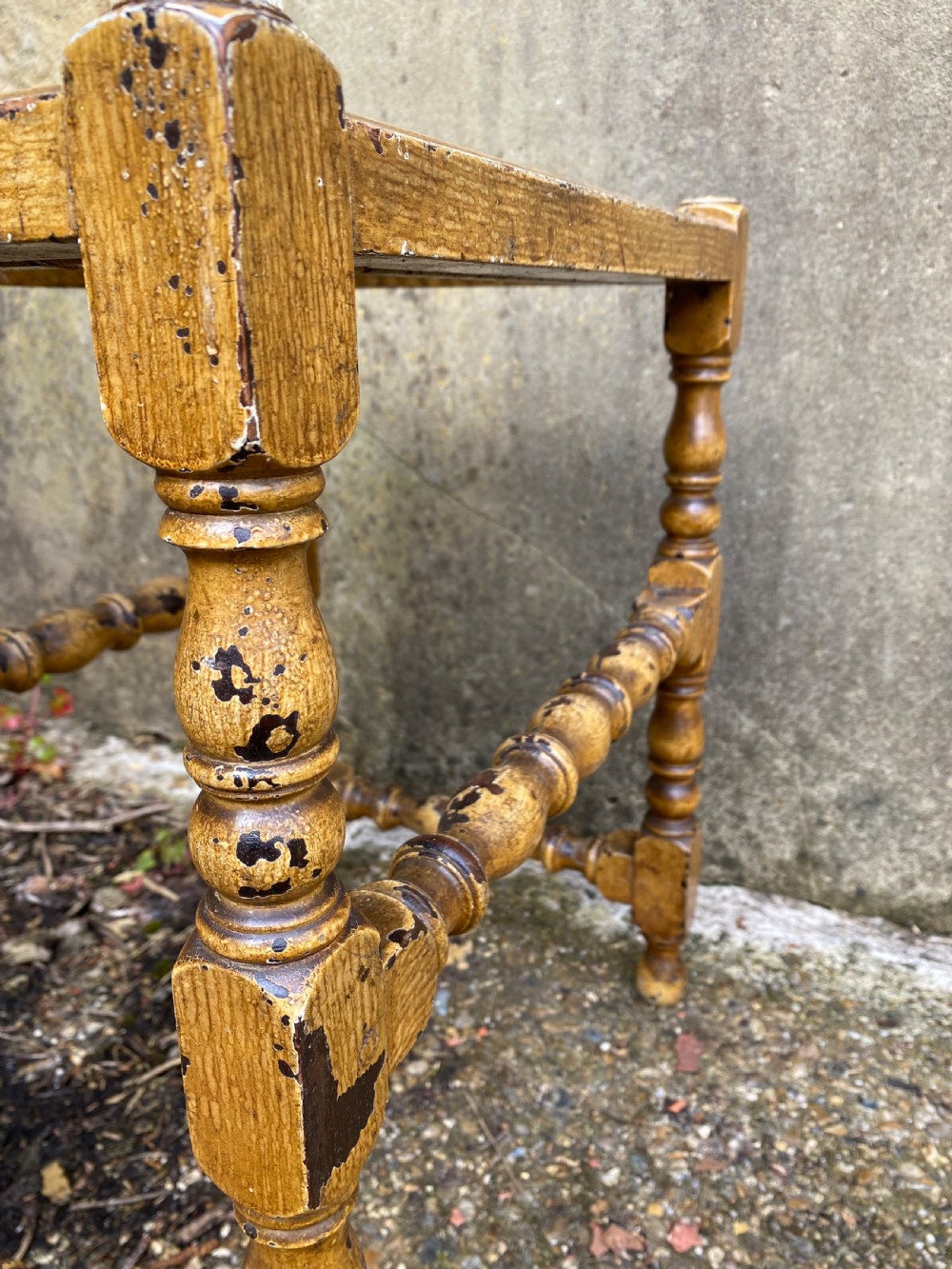 A rectangular wooden stool featuring turned bobbin legs, horizontal stretchers, and a woven cane seat panel with a distressed warm brown finish. View XII