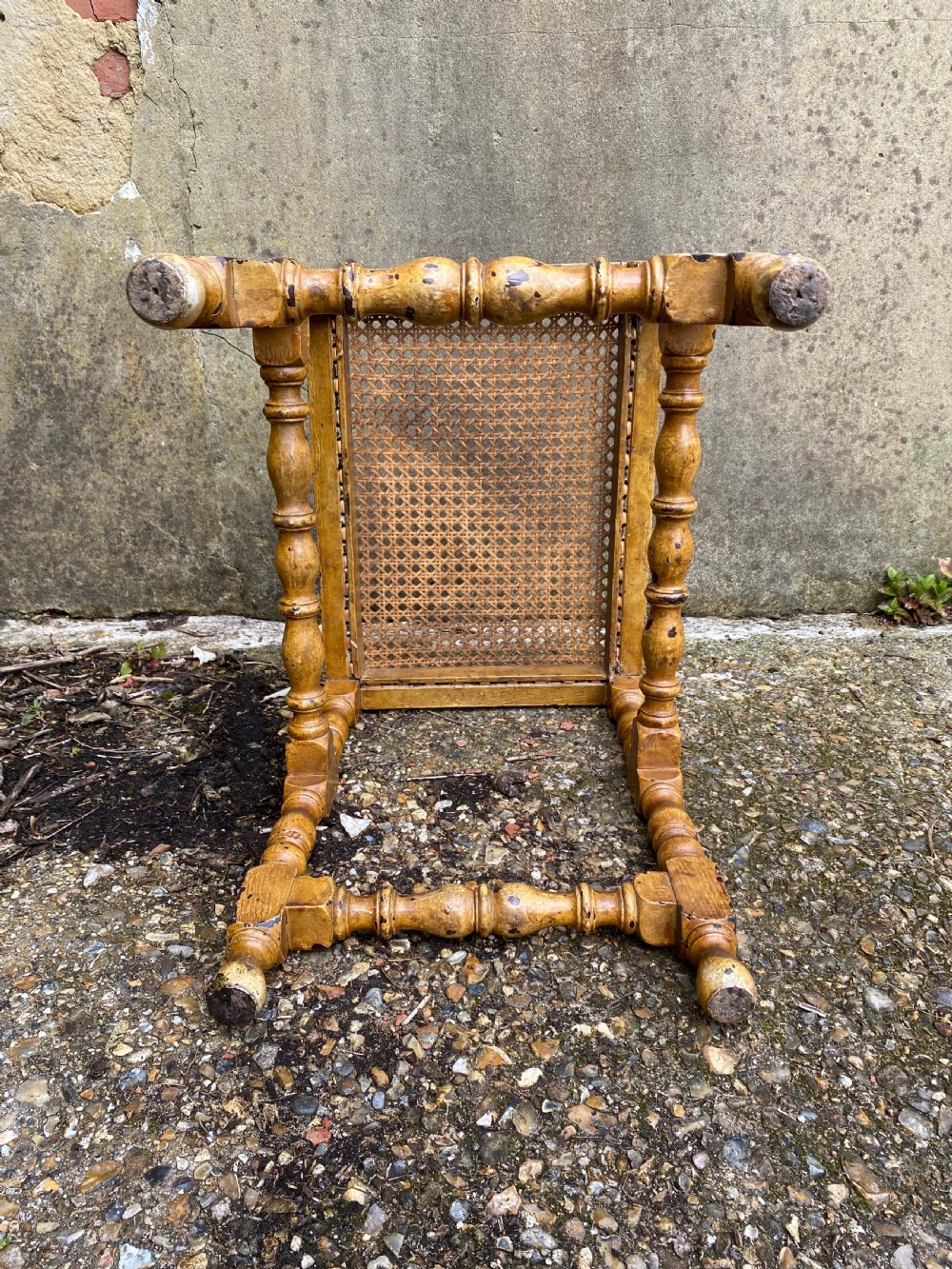 A rectangular wooden stool featuring turned bobbin legs, horizontal stretchers, and a woven cane seat panel with a distressed warm brown finish. View XV