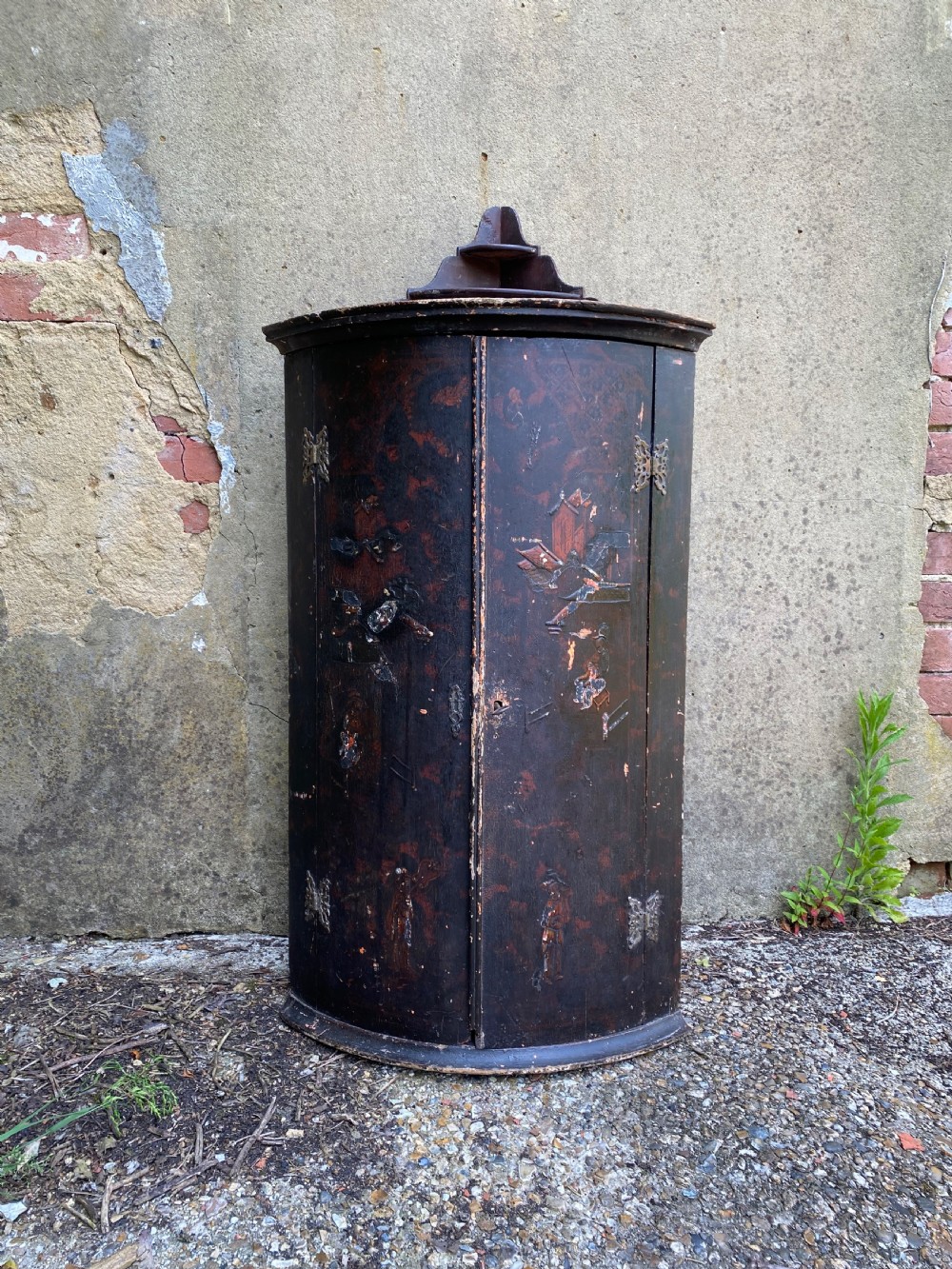 A dark lacquered Georgian corner cupboard featuring hand-painted Chinoiserie figures, architectural motifs, and brass butterfly hinges.