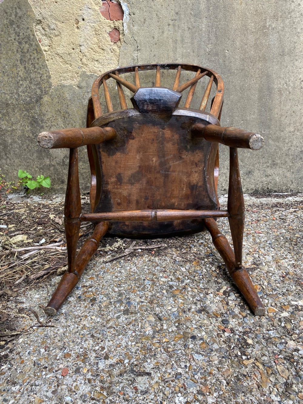 An antique wooden Windsor armchair with a stick-back design and a sculpted wooden seat stands against a weathered wall. View XV