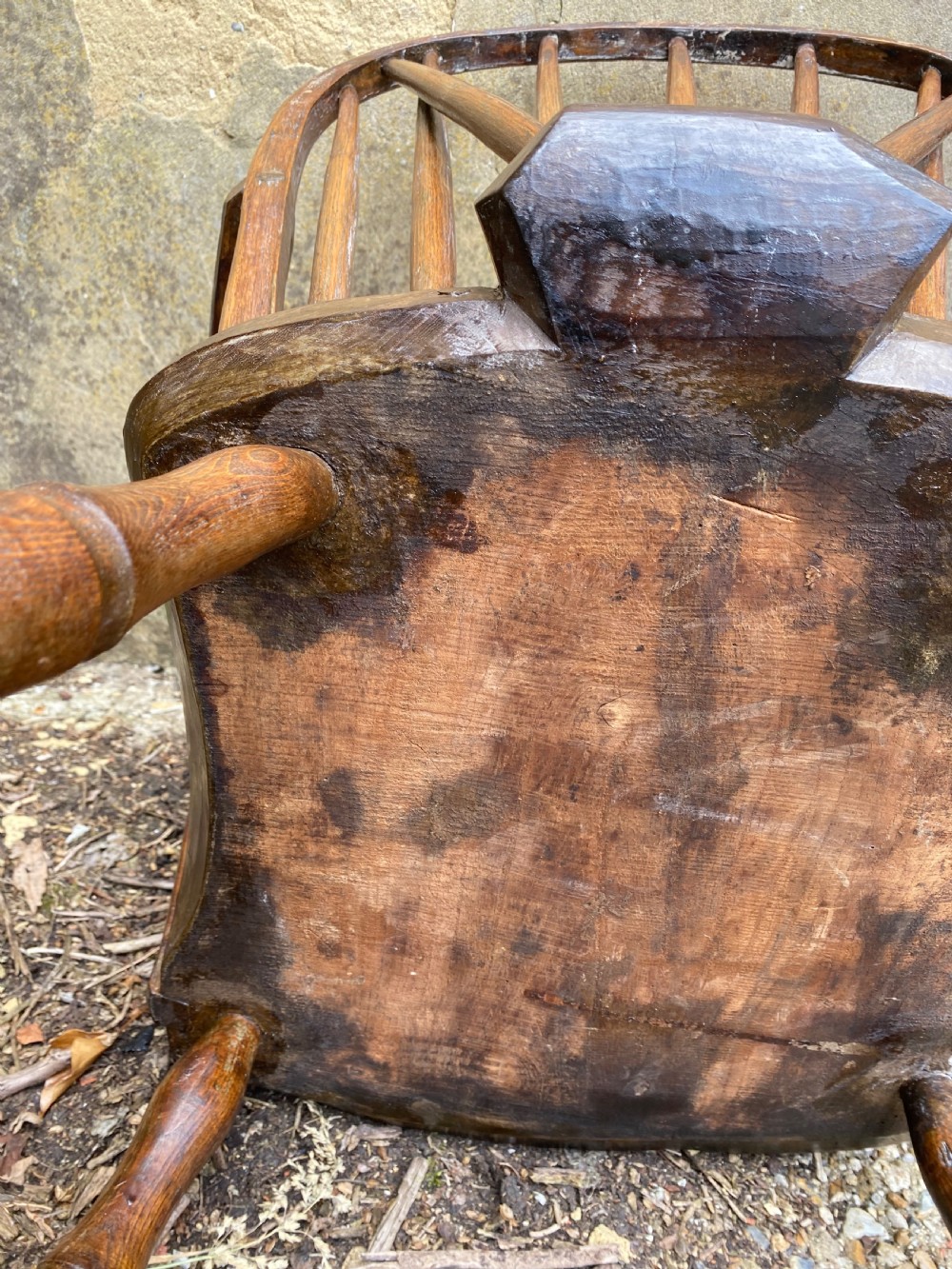 An antique wooden Windsor armchair with a stick-back design and a sculpted wooden seat stands against a weathered wall. View XVI