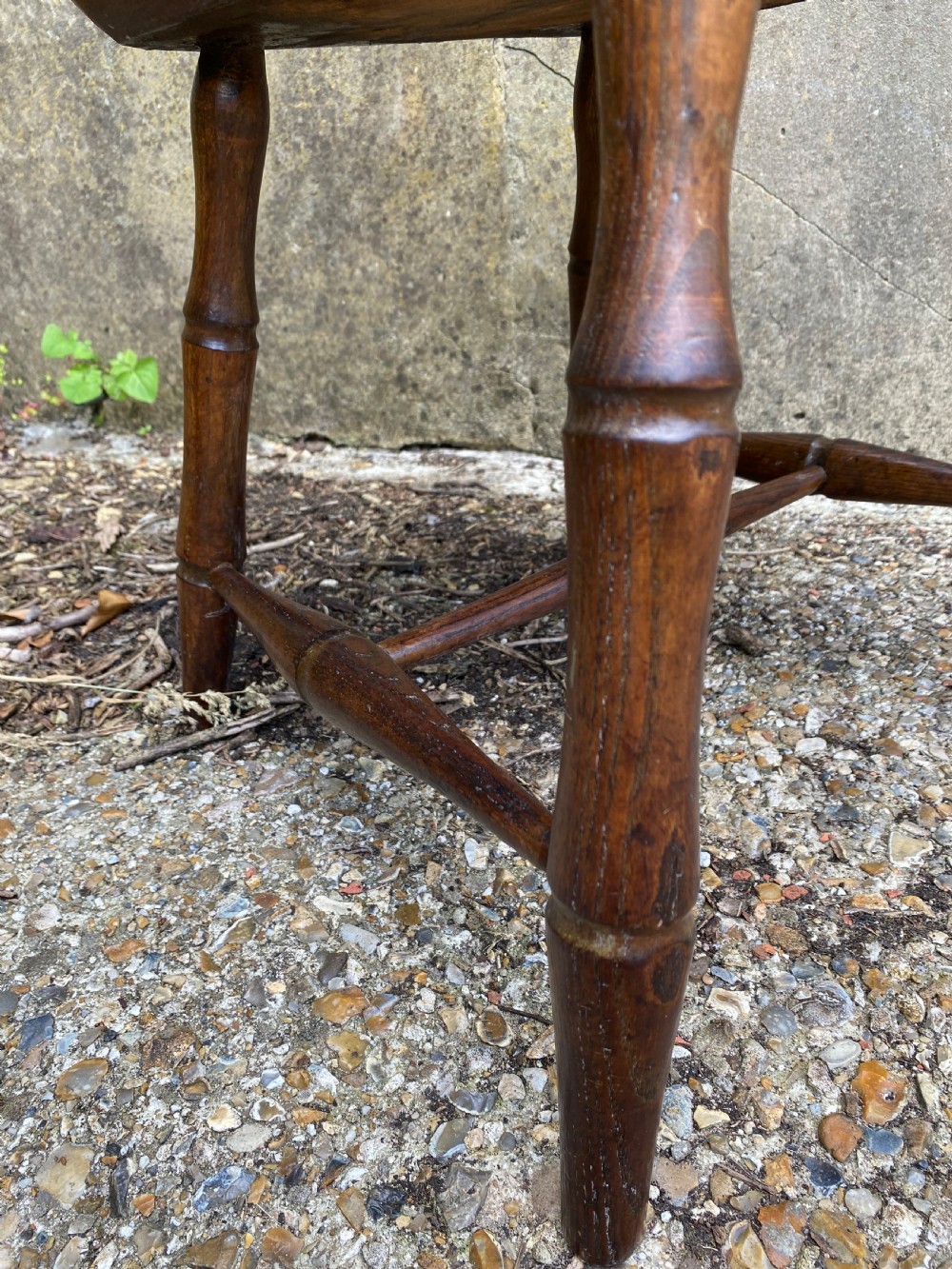 An antique wooden Windsor armchair with a stick-back design and a sculpted wooden seat stands against a weathered wall. View XIX