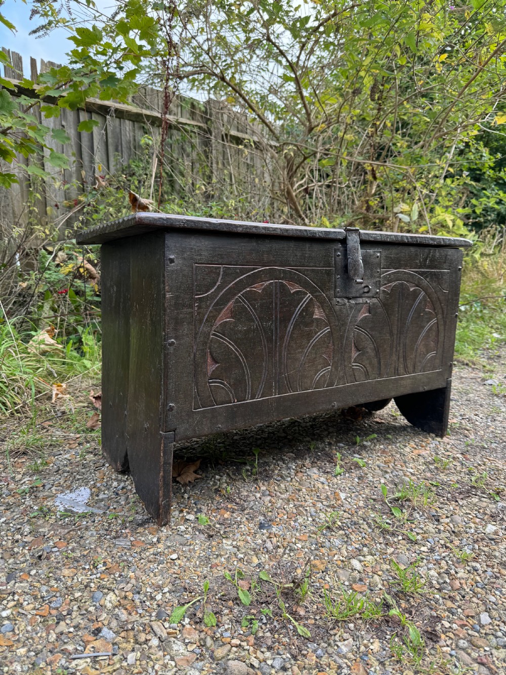 A small dark oak coffer featuring a carved top frieze, a three-panel front, and a central iron escutcheon. View III