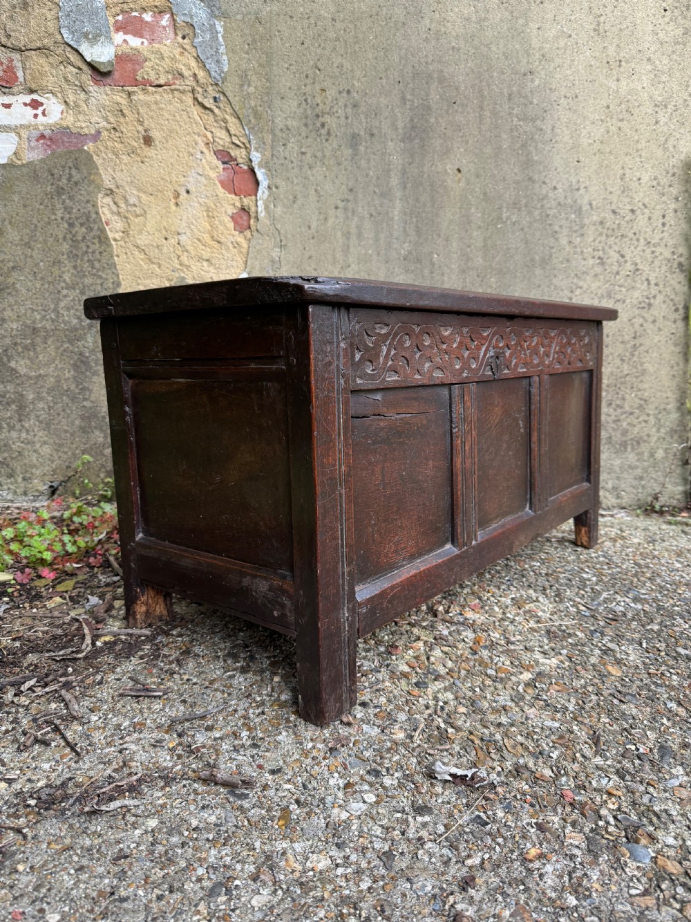 A small dark oak coffer featuring a carved top frieze, a three-panel front, and a central iron escutcheon. View IV
