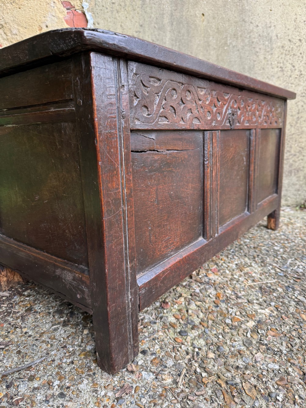 A small dark oak coffer featuring a carved top frieze, a three-panel front, and a central iron escutcheon. View VIII