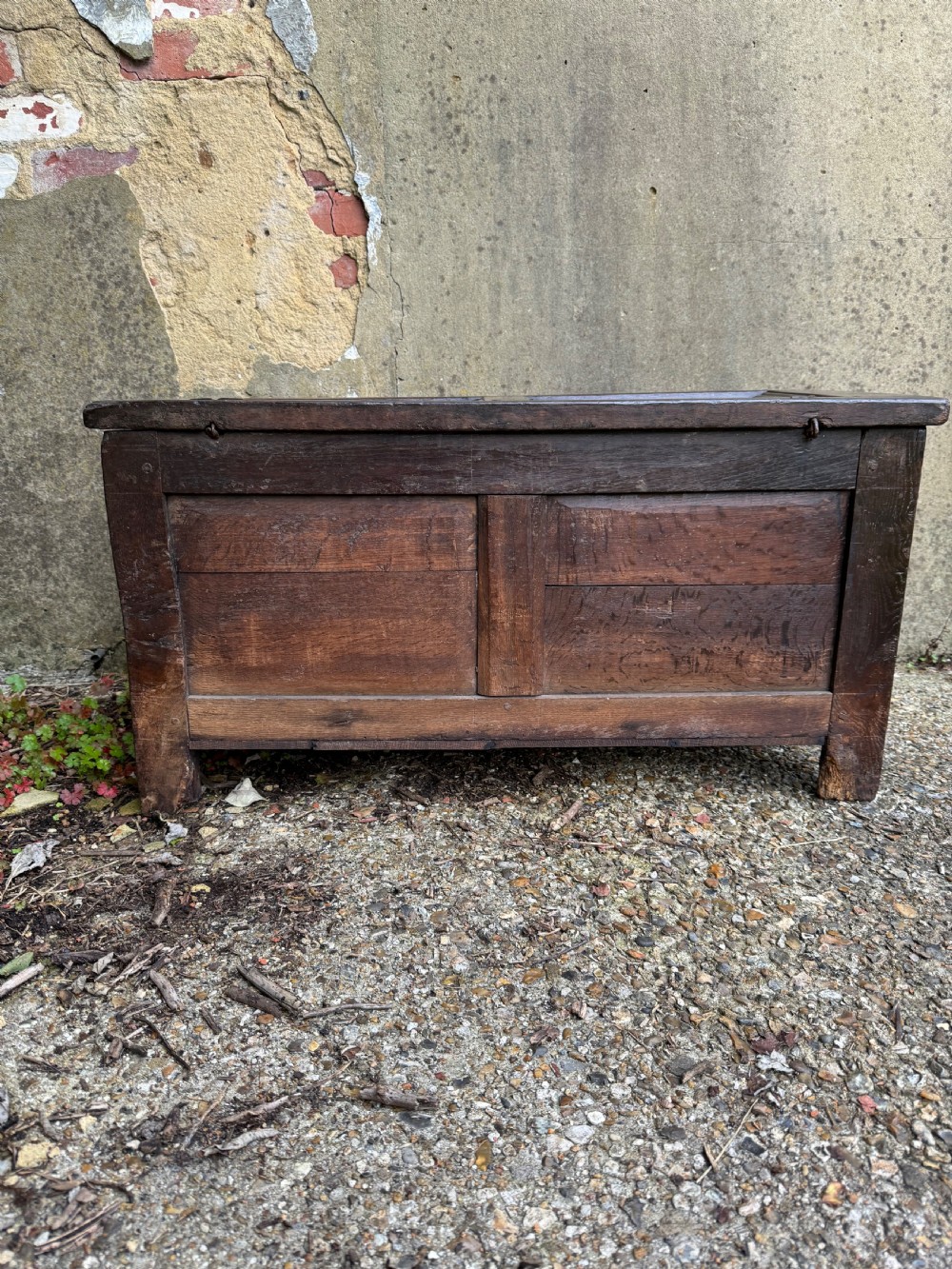 A small dark oak coffer featuring a carved top frieze, a three-panel front, and a central iron escutcheon. View X