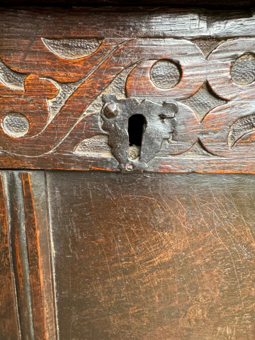 A small dark oak coffer featuring a carved top frieze, a three-panel front, and a central iron escutcheon. View XI