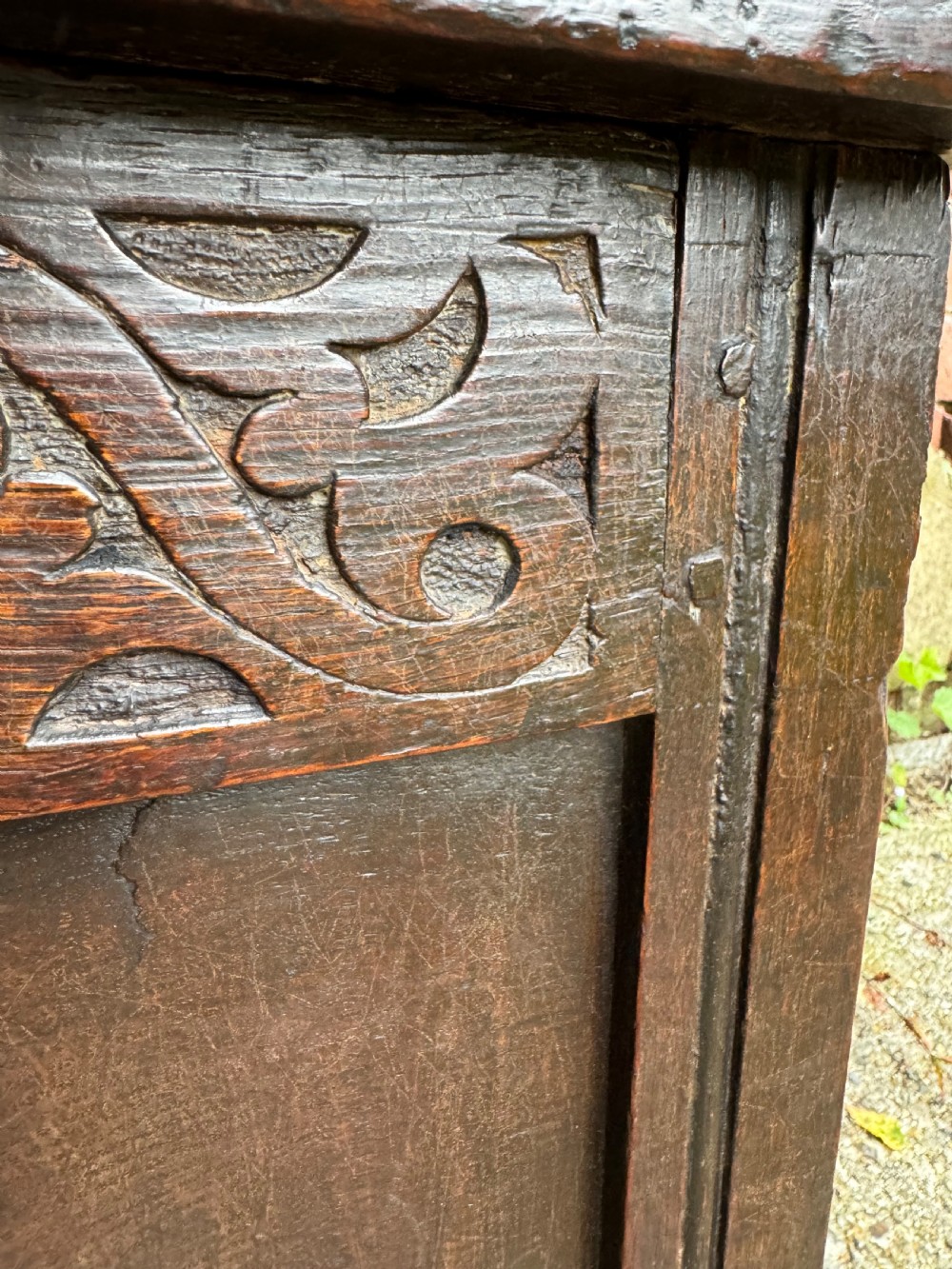 A small dark oak coffer featuring a carved top frieze, a three-panel front, and a central iron escutcheon. View XII