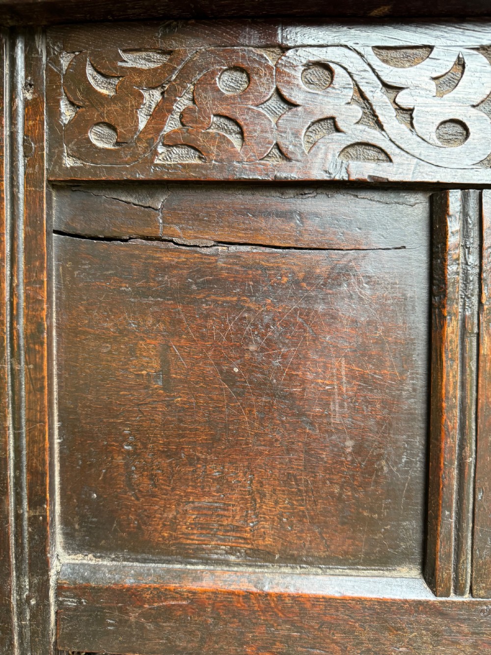 A small dark oak coffer featuring a carved top frieze, a three-panel front, and a central iron escutcheon. View XIII