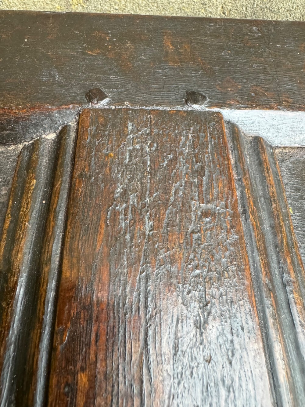 A small dark oak coffer featuring a carved top frieze, a three-panel front, and a central iron escutcheon. View XVI