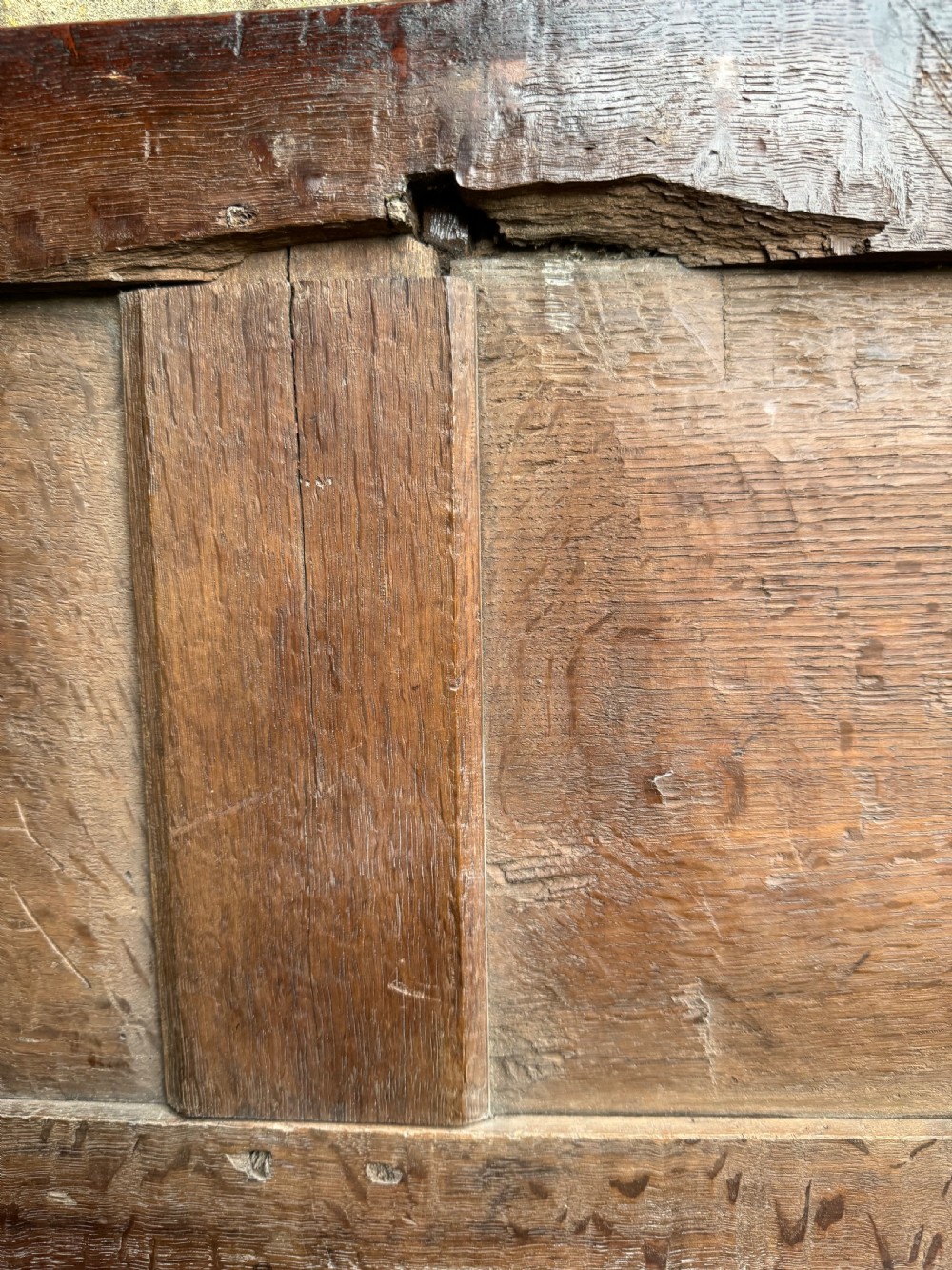 A small dark oak coffer featuring a carved top frieze, a three-panel front, and a central iron escutcheon. View XX
