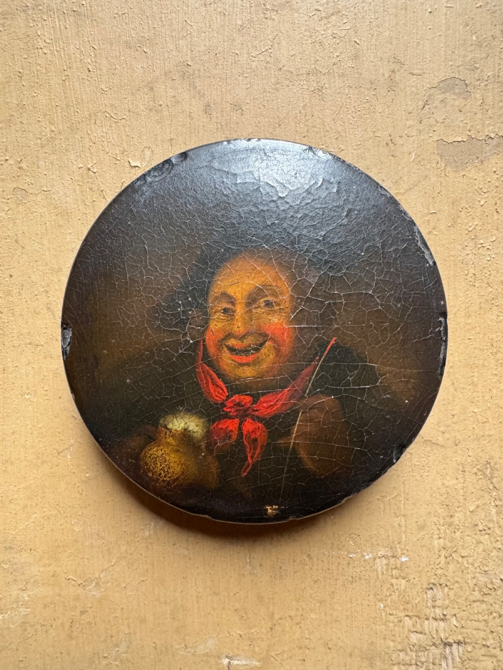 A circular antique lacquer portrait box lid depicting a smiling man with a red neckerchief featuring visible surface craquelure.