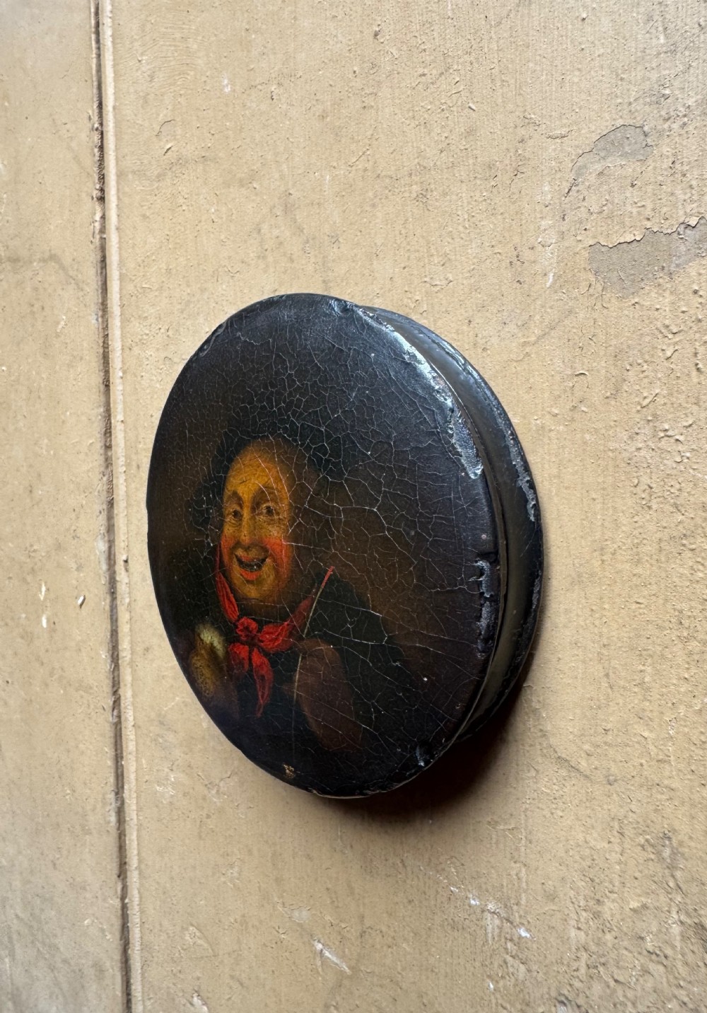 A circular antique lacquer portrait box lid depicting a smiling man with a red neckerchief featuring visible surface craquelure. View V