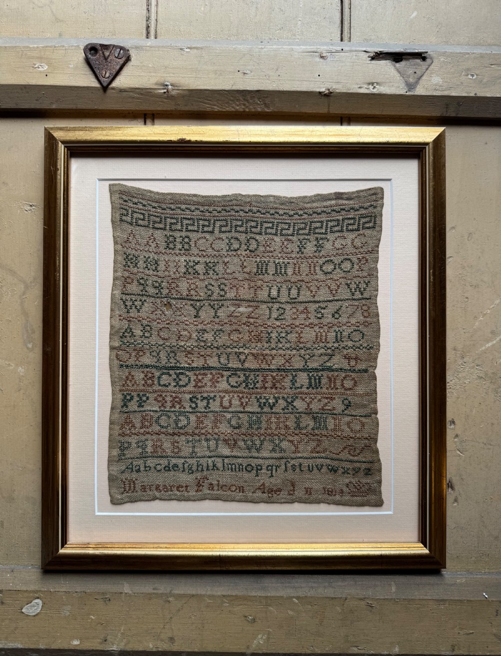 A framed nineteenth-century needlework sampler stitched with alphabet rows, numbers, and a signature on a natural linen ground within a gilded frame.