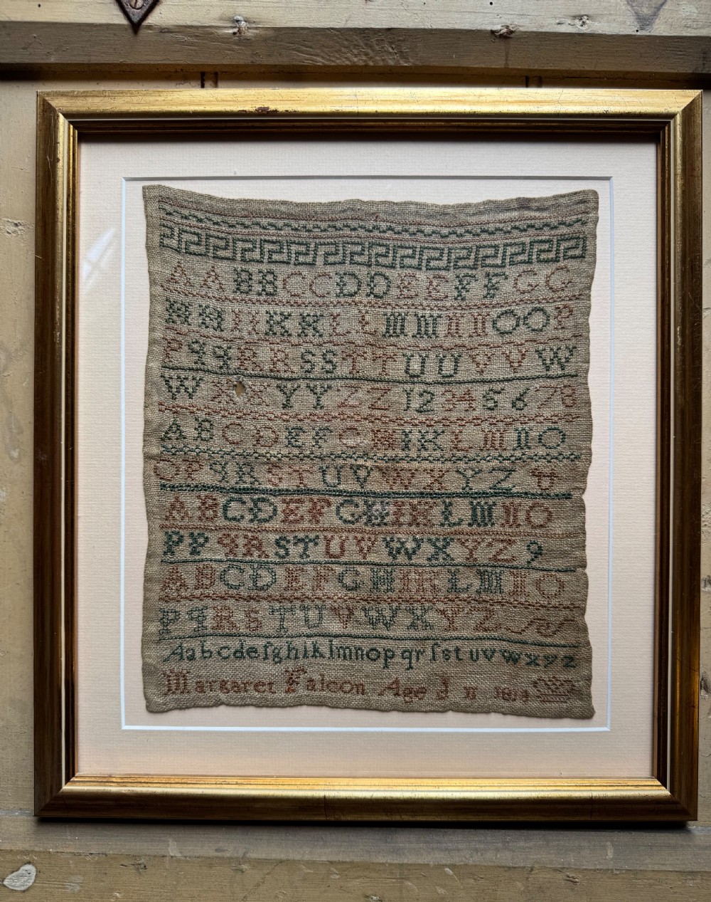 A framed nineteenth-century needlework sampler stitched with alphabet rows, numbers, and a signature on a natural linen ground within a gilded frame. View II