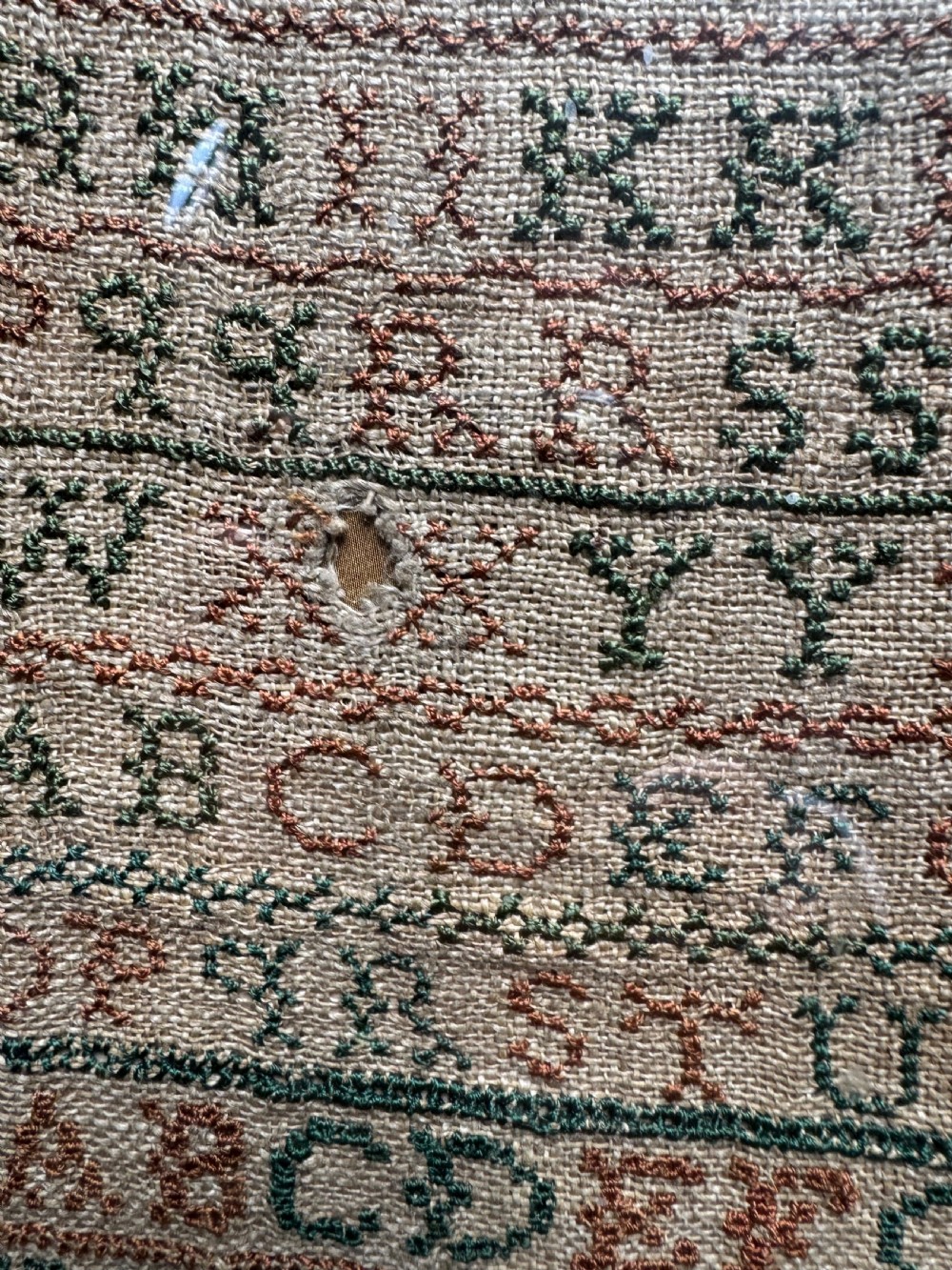 A framed nineteenth-century needlework sampler stitched with alphabet rows, numbers, and a signature on a natural linen ground within a gilded frame. View III
