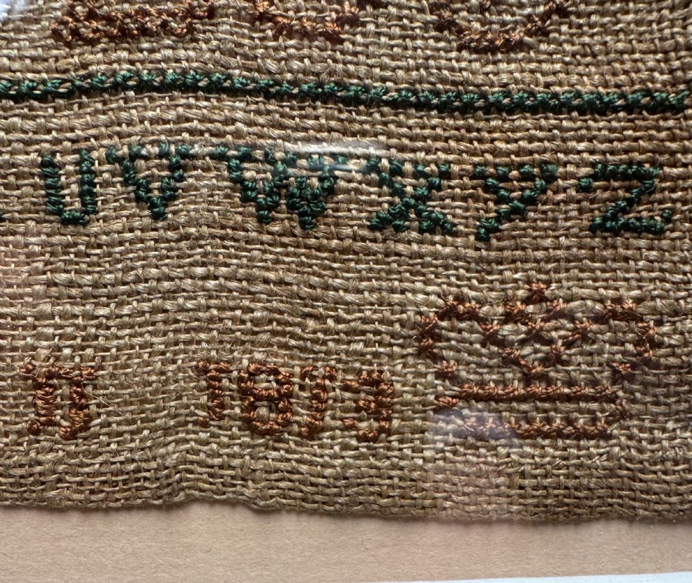A framed nineteenth-century needlework sampler stitched with alphabet rows, numbers, and a signature on a natural linen ground within a gilded frame. View IV