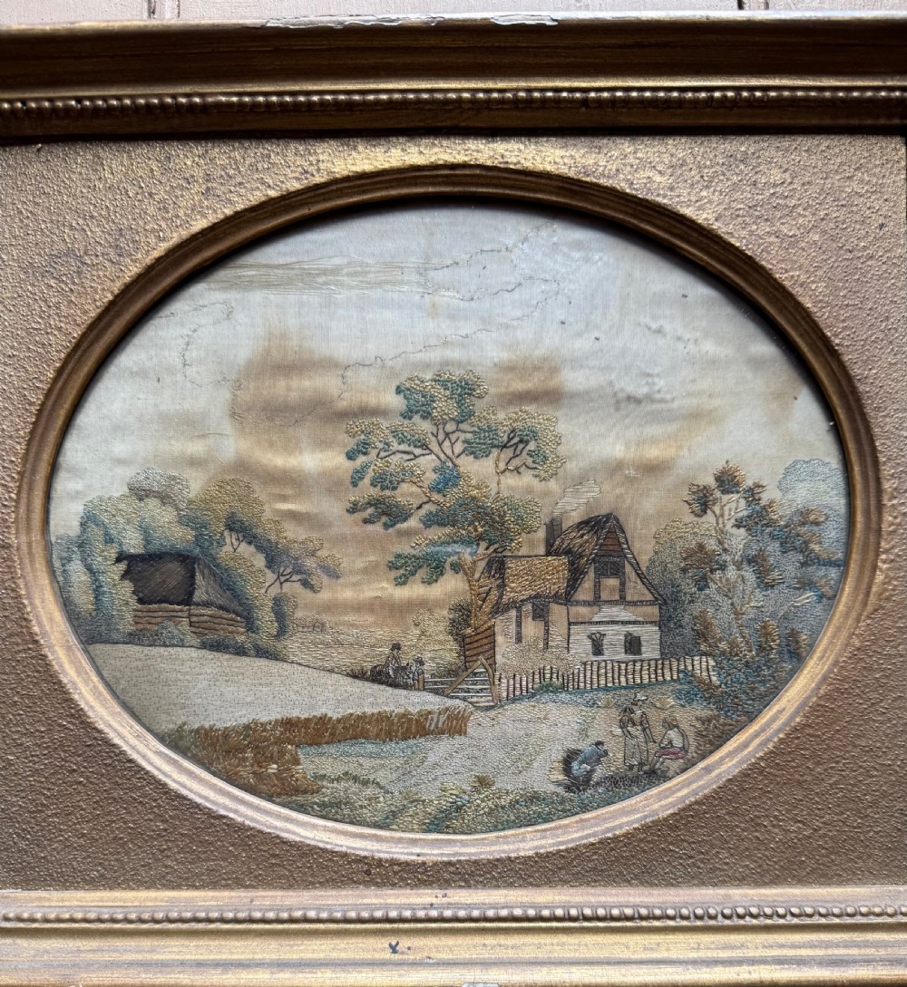 A framed rectangular gold gilded picture frame featuring an oval aperture surrounding a hand-embroidered silk landscape scene with a cottage and trees. View III