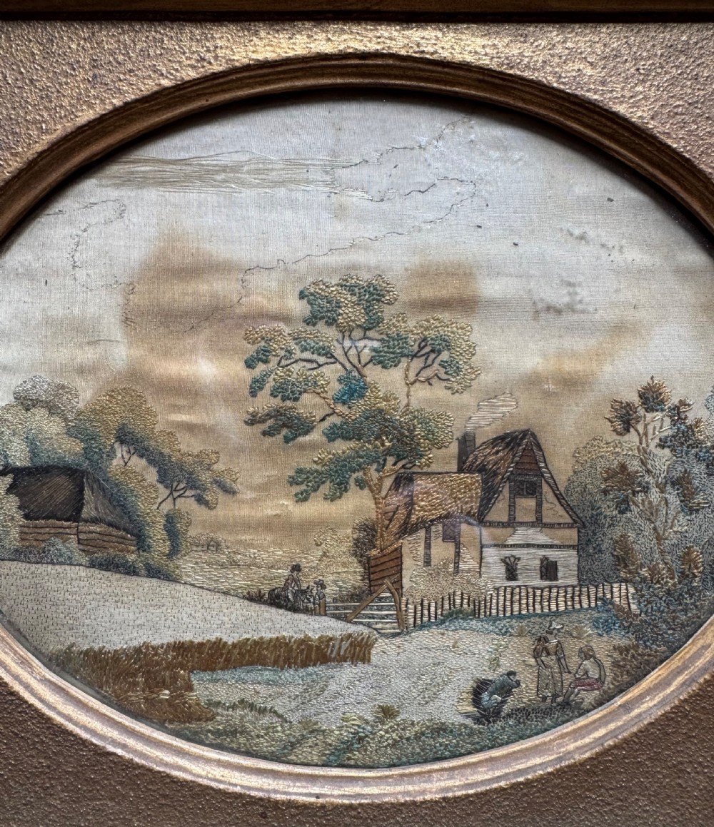 A framed rectangular gold gilded picture frame featuring an oval aperture surrounding a hand-embroidered silk landscape scene with a cottage and trees. View IV
