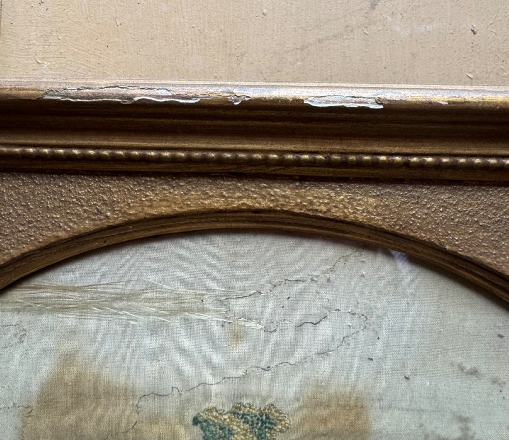 A framed rectangular gold gilded picture frame featuring an oval aperture surrounding a hand-embroidered silk landscape scene with a cottage and trees. View V