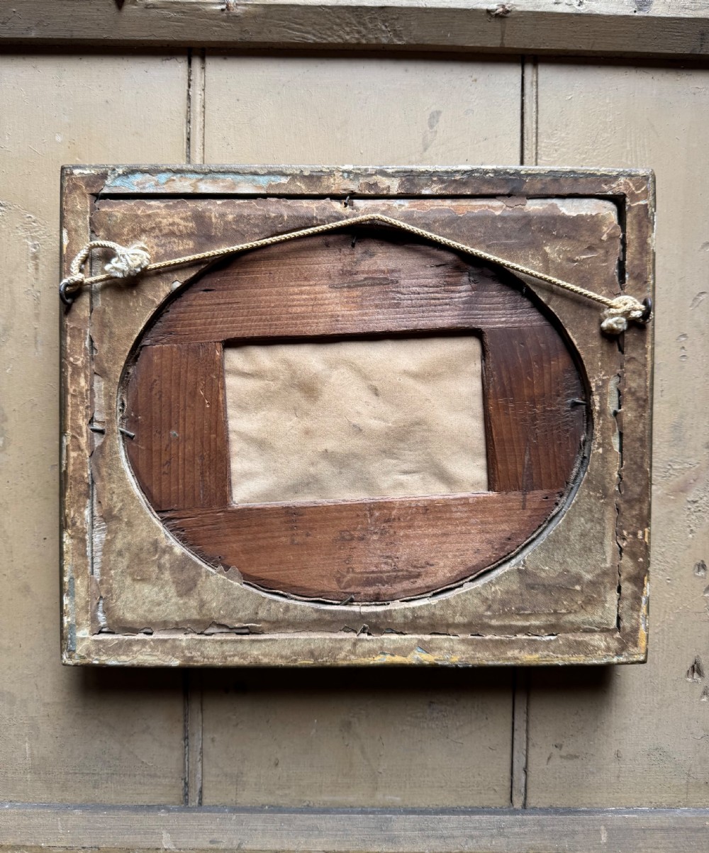 A framed rectangular gold gilded picture frame featuring an oval aperture surrounding a hand-embroidered silk landscape scene with a cottage and trees. View VII