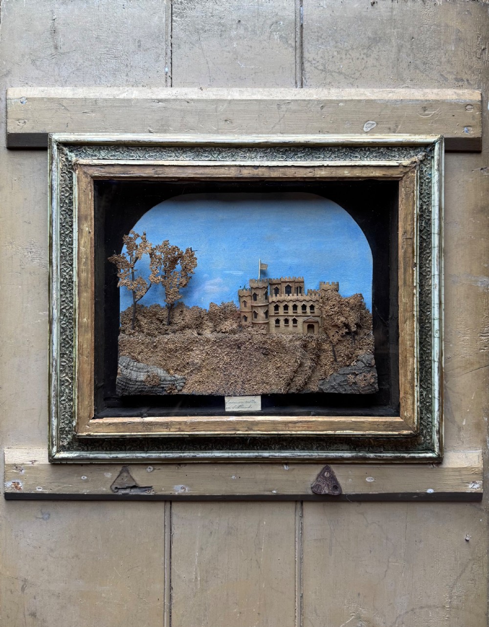 A framed nineteenth-century three-dimensional cork diorama depicting a castle on a hill against a painted light blue backdrop inside a glazed moulded frame.
