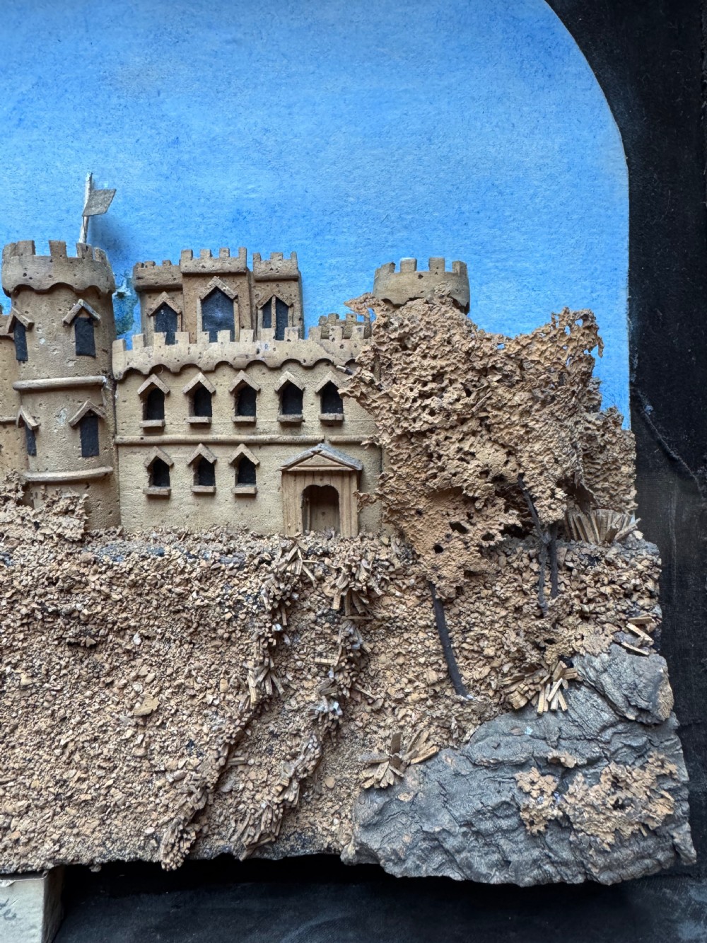 A framed nineteenth-century three-dimensional cork diorama depicting a castle on a hill against a painted light blue backdrop inside a glazed moulded frame. View III