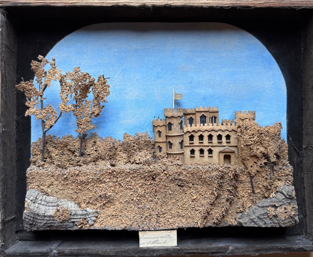 A framed nineteenth-century three-dimensional cork diorama depicting a castle on a hill against a painted light blue backdrop inside a glazed moulded frame. View IV